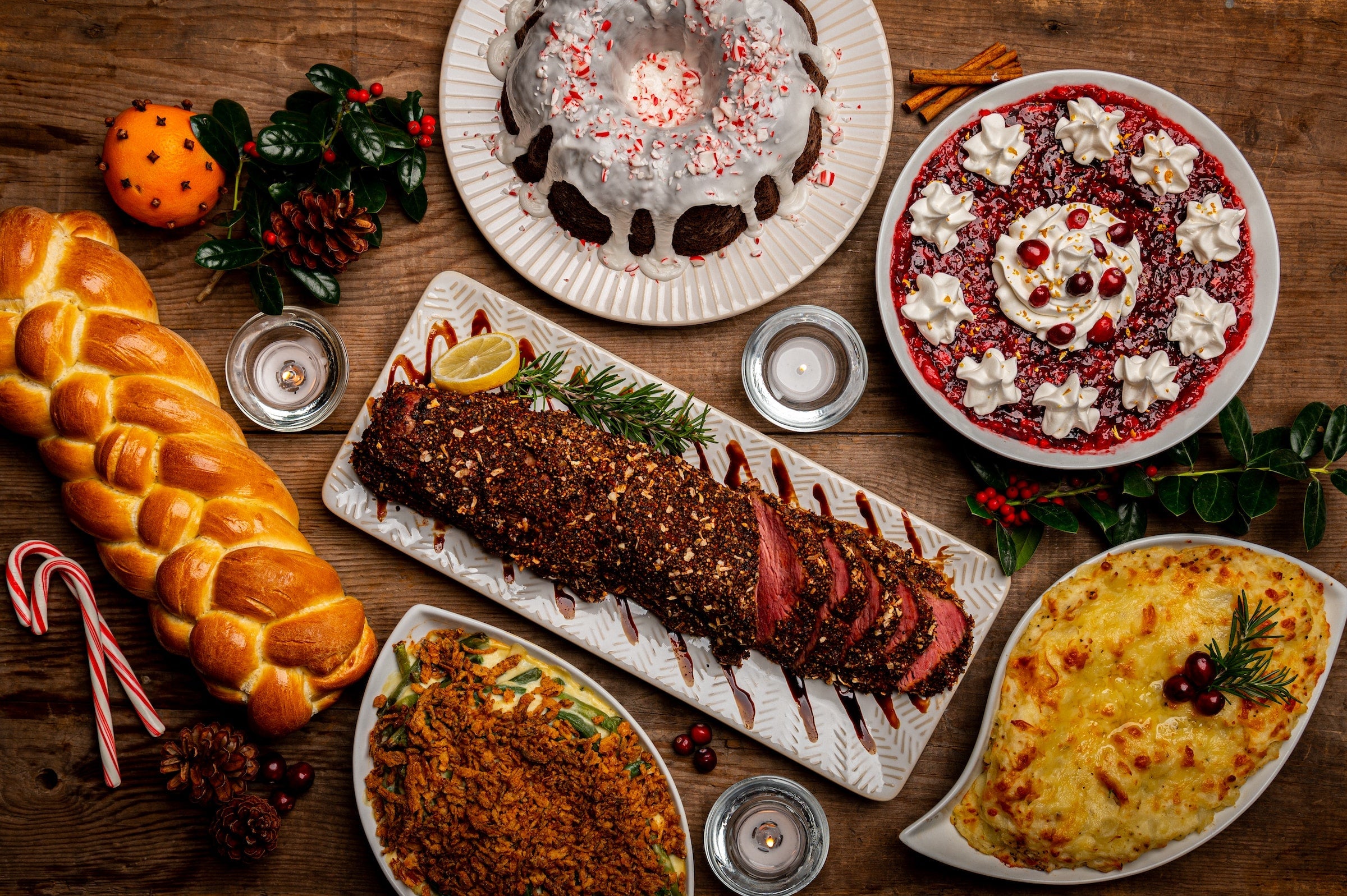 This is a large holiday-themed feast. There is a challah bread, a well-seasoned pork loin, figgy pudding, a potato dish, green bean casserole, and a peppermint bundt cake. 
